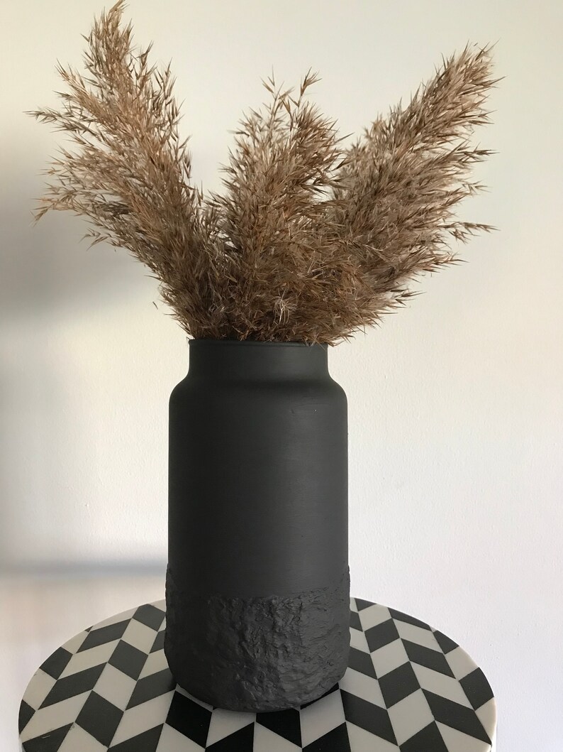 May include: A black vase with a textured bottom, filled with dried pampas grass.