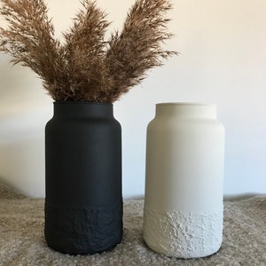 May include: Two ceramic vases, one black and one white, with a textured bottom. Both vases are filled with dried pampas grass.