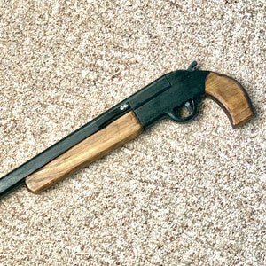 May include: A black and wood-toned toy shotgun. The toy gun features a black barrel and receiver with wooden hand grips and forend. The toy gun is a replica of a classic shotgun design.