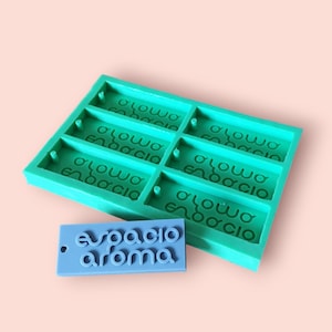 Puede incluir: Un molde de silicona turquesa con seis cavidades rectangulares, cada una estampada con el texto "olowo enbaccio". También se muestra una etiqueta rectangular azul con el texto "espacio aroma".