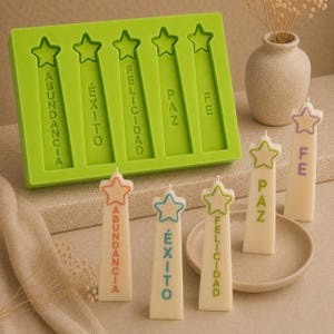 May include: A lime green silicone mold with five star-topped rectangular cavities, each embossed with the Spanish words Abundancia, Éxito, Felicidad, Paz, and Fe. Five off-white pillar candles stand nearby, each featuring a colored star and matching text.