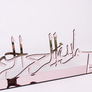 May include: A rose gold mirrored acrylic wall decor with the Arabic phrase "Mashallah" in a decorative font.