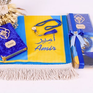 May include: A prayer mat in blue and yellow, featuring the name "Amir" in English and Arabic script, alongside a blue velvet Quran and a blue beaded tasbih. The set is presented with a blue ribbon.