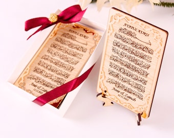 Könnte beinhalten: Eine Holzplakette mit arabischer Kalligraphie und dem Text "Ayatul Kursi" und "Amir & Zainab 12.12.2022". Die Plakette steht auf einem kleinen Holzständer und befindet sich in einer weißen Schachtel mit einem roten Band.