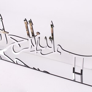 May include: A silver mirrored acrylic wall decor with the Arabic phrase "Bismillah" in a decorative font.
