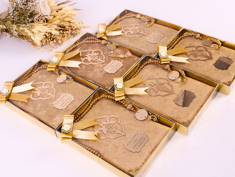 May include: Set of five gold gift boxes with gold ribbon and a gold prayer beads inside each box. Each box has a gold-colored wooden cutout of a heart with Arabic calligraphy and a personalized name tag.