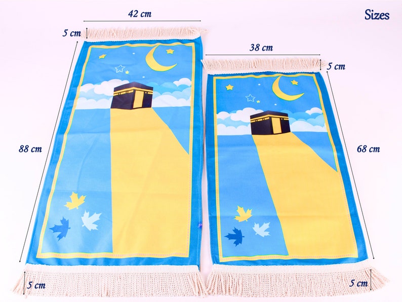 May include: Two prayer mats with a blue and yellow design featuring the Kaaba, a crescent moon, and stars. The larger mat is 88 cm long and 42 cm wide, the smaller one is 68 cm long and 38 cm wide. Both have fringed edges.