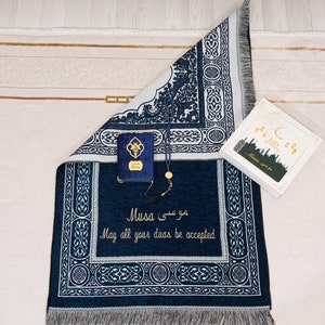 May include: A navy blue prayer mat with white detailing, featuring Arabic script and the English phrase "May all your duas be accepted." Includes a small blue book, prayer beads, and a gift box with "Eid Mubarak" text.