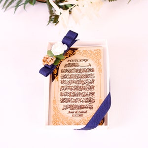 May include: A wooden plaque with gold lettering and a blue ribbon. The plaque features the Arabic text of Ayatul Kursi, a verse from the Quran, and is personalized with the names "Amir & Zainab" and the date "12.12.2022".
