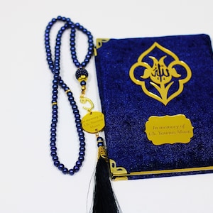 K&ouml;nnte beinhalten: Ein Gebetsbuch aus blauem Samt mit goldenen Verzierungen und einer goldenen Inschrift mit dem Text "In memory of Ch. Younus Maan". Neben dem Buch liegt eine blaue Gebetskette mit einem goldenen Anh&auml;nger.