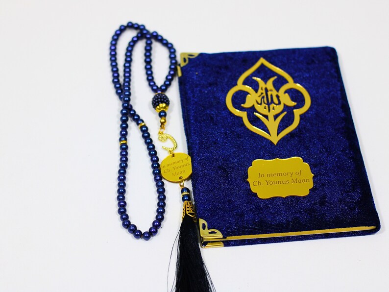 K&ouml;nnte beinhalten: Ein Gebetsbuch aus blauem Samt mit goldenen Verzierungen und einer goldenen Inschrift mit dem Text "In memory of Ch. Younus Maan". Neben dem Buch liegt eine blaue Gebetskette mit einem goldenen Anh&auml;nger.
