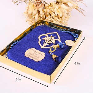 May include: A gold box containing a blue prayer mat, a beaded rosary, and a decorative gold pendant. The box is 5 inches wide and 6 inches long. The box also contains a small gold plaque with Arabic text.