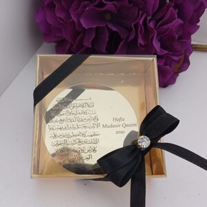 Op de afbeelding: Een gouden geschenkdoos met een zwart lint en een ronde, gouden plaquette met Arabische kalligrafie en de tekst "Hafiz Mudasir Qasim 2021".