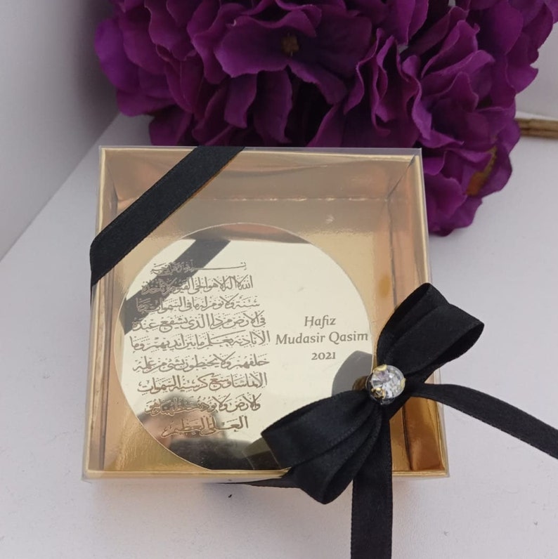 Op de afbeelding: Een gouden geschenkdoos met een zwart lint en een ronde, gouden plaquette met Arabische kalligrafie en de tekst "Hafiz Mudasir Qasim 2021".