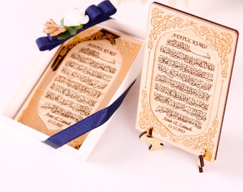 Könnte beinhalten: Eine Holzplakette mit goldenem Design und arabischer Kalligraphie. Die Plakette ist mit dem Text "Ayatul Kursi" und den Namen "Amir & Zainab" sowie dem Datum "12.12.2022" graviert. Die Plakette steht auf einem kleinen Holzständer.