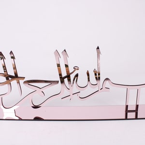 May include: A rose gold mirrored wall decor with the Arabic phrase "Bismillah" in a decorative font.