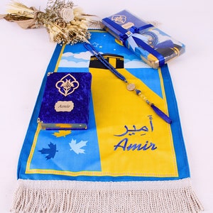 May include: A blue and yellow prayer mat with the name "Amir" embroidered in blue. A blue velvet Quran with gold accents and a matching prayer bead set are included. A gift set with a floral arrangement.