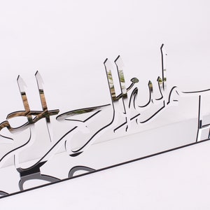 May include: A silver mirrored acrylic wall decor with the Arabic phrase "Mashallah" in a decorative font.