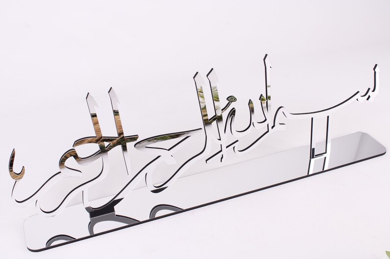 May include: A silver mirrored acrylic wall decor with the Arabic phrase "Mashallah" in a decorative font.