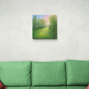 Puede incluir: Arte en lienzo cuadrado que representa un sendero forestal soleado. La pintura presenta un prado verde vibrante que conduce a una abertura brillante y soleada. Los &aacute;rboles bordean el camino, con un cielo azul y rosa visible arriba.