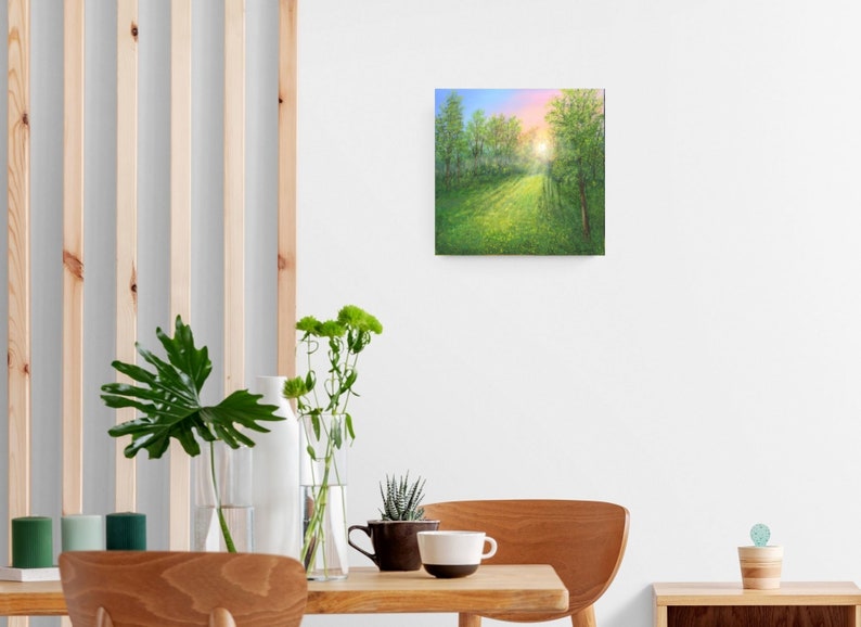 Puede incluir: Cuadro cuadrado que representa una escena de bosque soleado. La pintura muestra un camino que conduce a la distancia, rodeado de &aacute;rboles verdes y un campo de flores amarillas. El cielo pasa del azul al rosa, sugiriendo el amanecer o el atardecer.