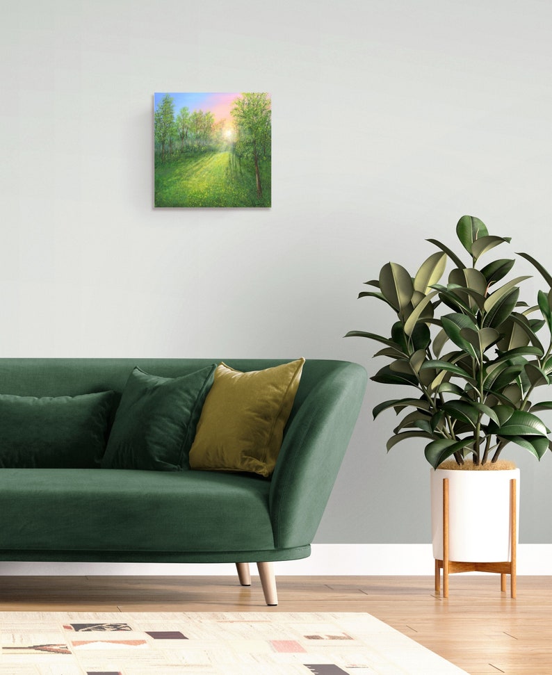 Puede incluir: Arte en lienzo cuadrado que representa un camino soleado a trav&eacute;s de un prado verde y &aacute;rboles. La obra de arte presenta una vibrante paleta de colores verdes, azules y rosas, creando una escena de paisaje serena. La pintura se exhibe sobre un sof&aacute; verde.