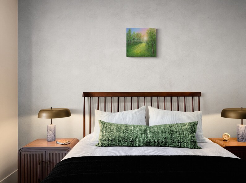 Puede incluir: Una pintura cuadrada que representa un paisaje con un camino que conduce a un bosque. La obra de arte est&aacute; colgada sobre una cama con ropa de cama blanca, un coj&iacute;n verde y una manta negra. Dos l&aacute;mparas con bases de m&aacute;rmol flanquean la cama.