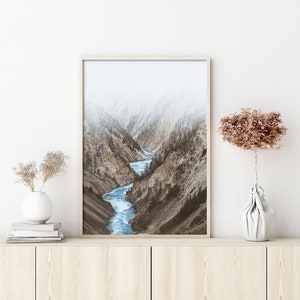 May include: A framed photograph of a river winding through a misty mountain canyon. The river is a bright blue, and the mountains are a muted brown and gray.