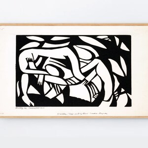 May include: A framed black and white abstract print. The artwork depicts stylized figures in a wrestling or embracing pose, with a background of organic shapes. The print is mounted in a light-colored wooden frame.