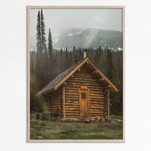 Könnte beinhalten: Eine Holzhütte mit einer braunen Tür steht auf einer Lichtung in einem Wald. Die Hütte ist von hohen Bäumen umgeben und im Hintergrund ist eine Bergkette zu sehen.