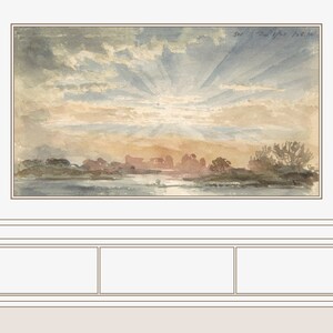 May include: A framed watercolor painting of a sunset over a body of water with a town in the distance. The painting is hanging on a wall above a brown wooden cabinet with three drawers.