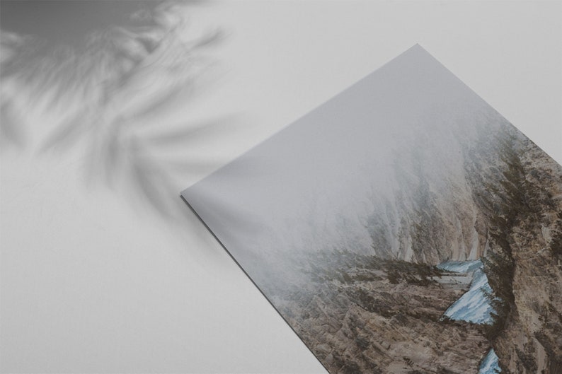 May include: A photograph of a mountain range with a narrow valley in the center. The valley is filled with fog and the mountains are covered in snow. The image is taken from a low angle, looking up at the mountains.