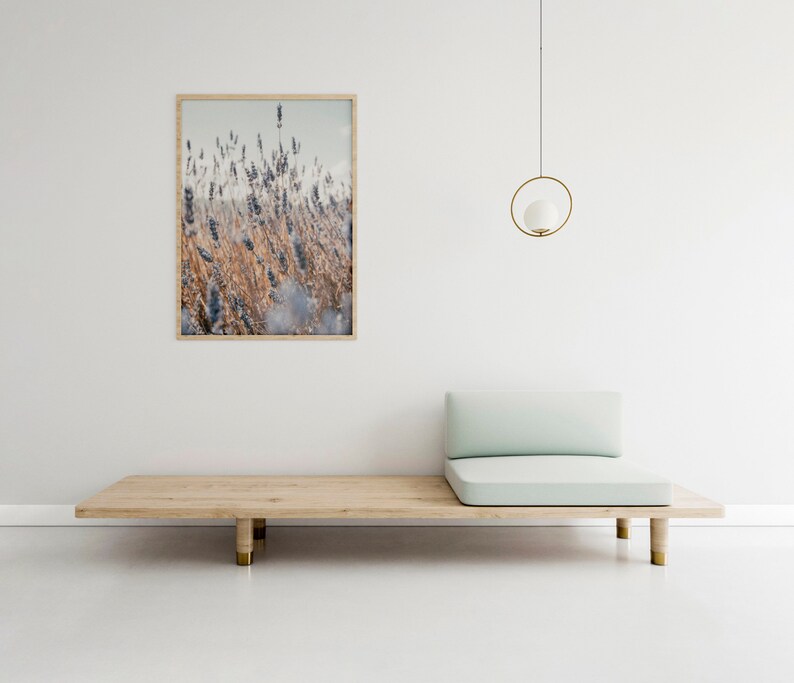 May include: A light wood platform bed with a light blue cushion and a framed print of lavender flowers hanging on a white wall. A gold pendant light hangs above the bed.