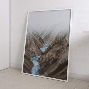 May include: A framed photograph of a river winding through a mountain valley. The mountains are covered in snow and fog, and the river is a bright blue.