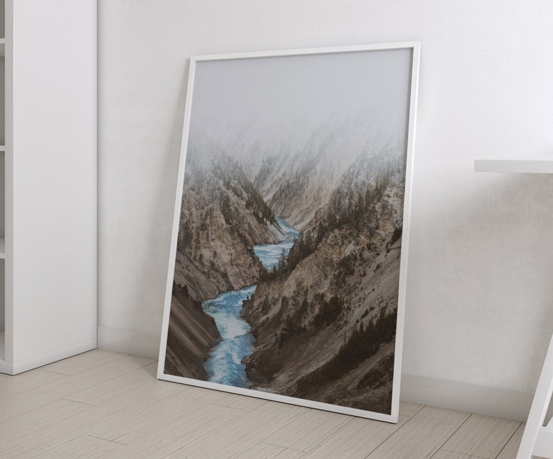 May include: A framed photograph of a river winding through a mountain valley. The mountains are covered in snow and fog, and the river is a bright blue.