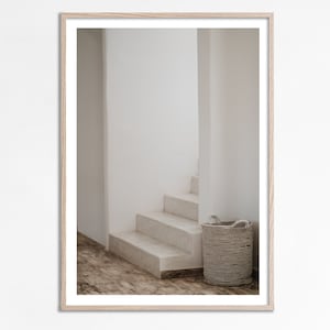 Könnte beinhalten: Ein gerahmtes Foto einer weißen Treppe, die zu einer weißen Tür führt. Ein geflochtener Korb steht am Fuße der Treppe.