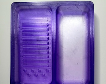 May include: A purple plastic tray with two compartments. One compartment has a series of small holes and the other compartment is empty.