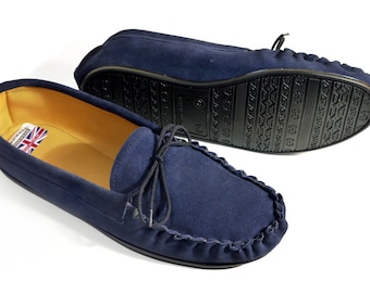 May include: A pair of navy blue suede moccasins with a leather sole and a decorative stitching detail around the edge. The moccasins have a lace-up closure and a Union Jack label on the inside.