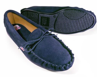 May include: A pair of navy blue suede moccasins with a leather sole and a decorative stitching detail around the edge. The moccasins have a small Union Jack flag on the side.