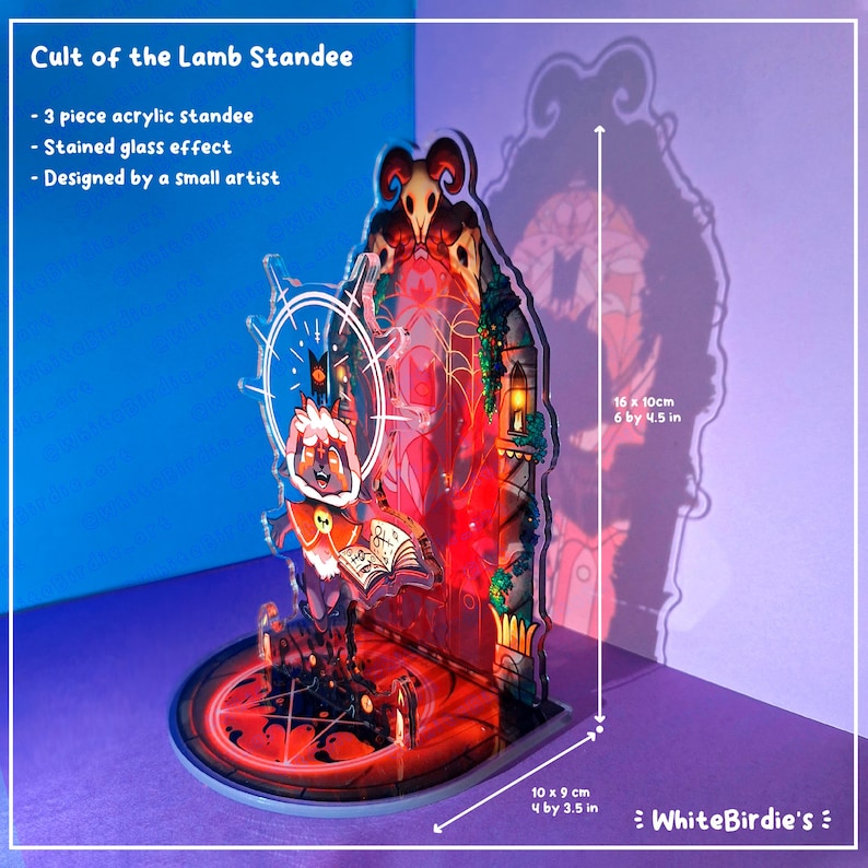 May include: A three-piece acrylic standee with a stained glass effect, featuring a design from Cult of the Lamb. The standee is 6 inches tall and 4.5 inches wide, with a base of 4 by 3.5 inches. The design includes a lamb character and a red and black color scheme.