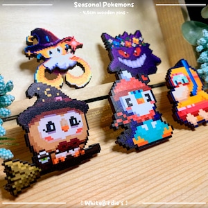 May include: Five wooden pins featuring pixel art designs of Pokemon characters. The pins are approximately 2.5 cm in size and feature a variety of colors, including red, blue, green, yellow, and black. The pins are labeled "Seasonal Pokemons - 2.5cm wooden pins - WhiteBirdies".