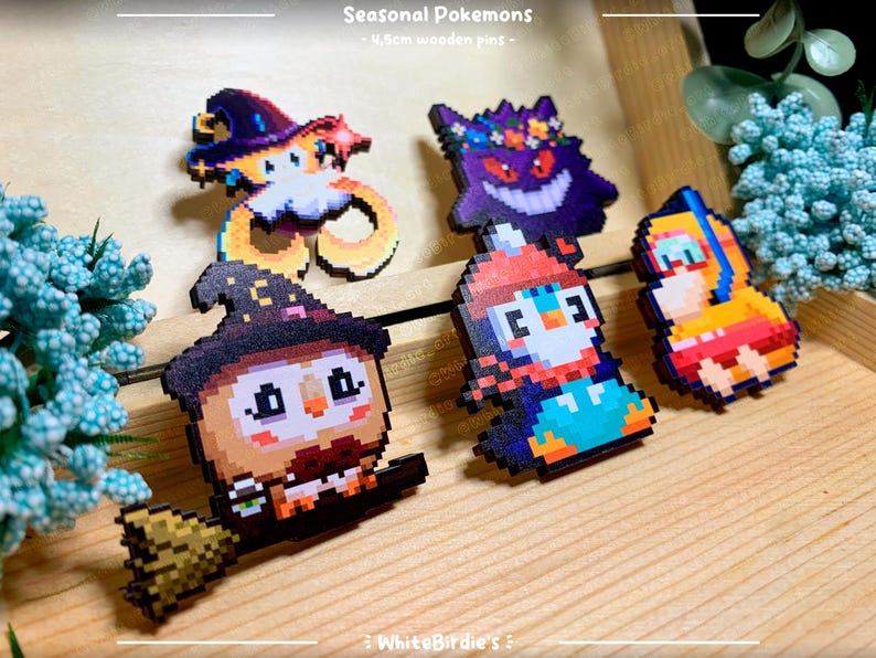 May include: Five wooden pins featuring pixel art designs of Pokemon characters. The pins are approximately 2.5 cm in size and feature a variety of colors, including red, blue, green, yellow, and black. The pins are labeled "Seasonal Pokemons - 2.5cm wooden pins - WhiteBirdies".