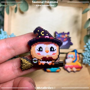 May include: A set of four 4.5cm wooden pins featuring pixel art designs of Pokemon characters. The pins are in a variety of colors, including black, white, red, yellow, and blue. The pins are displayed on a wooden surface. Seasonal Pokemons - 4.5cm wooden pins - WhiteBirdie's