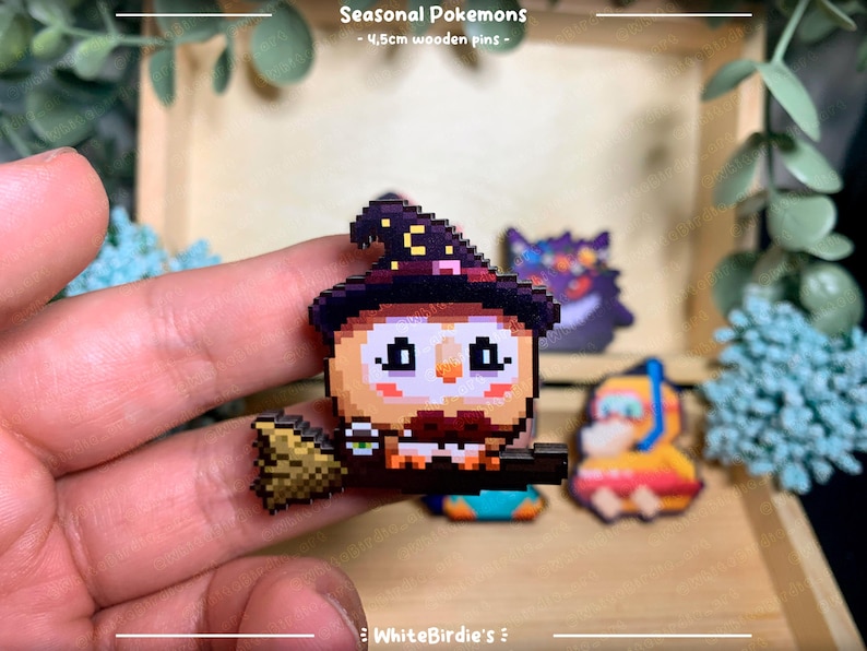 May include: A set of four 4.5cm wooden pins featuring pixel art designs of Pokemon characters. The pins are in a variety of colors, including black, white, red, yellow, and blue. The pins are displayed on a wooden surface. Seasonal Pokemons - 4.5cm wooden pins - WhiteBirdie's