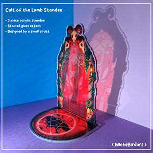 May include: A three-piece acrylic standee with a stained glass effect. The standee features a red and black design with a pentagram on the base and a gothic archway with a skull on top. The text "Cult of the Lamb Standee" is visible.