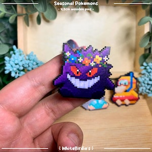 May include: A purple and black Gengar Pokemon pin with a flower crown. The pin is made of wood and is approximately 4.5cm in size. The pin is part of a collection of seasonal Pokemon pins.