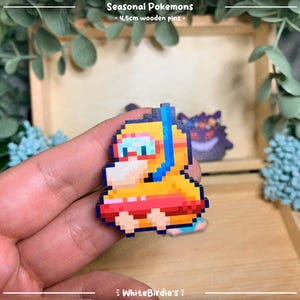 May include: A yellow and orange pixel art Pokemon character wearing a blue snorkel and goggles, floating on a red inner tube. The character is a wooden pin, approximately 4.5cm in size. The text "Seasonal Pokemons - 4.5cm wooden pins -" is visible above the character.