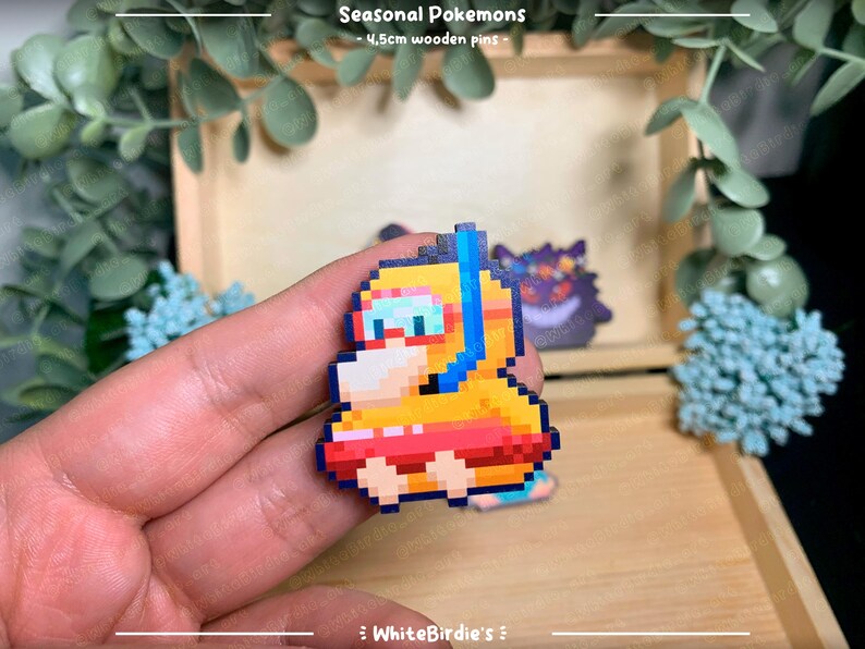 May include: A yellow and orange pixel art Pokemon character wearing a blue snorkel and goggles, floating on a red inner tube. The character is a wooden pin, approximately 4.5cm in size. The text "Seasonal Pokemons - 4.5cm wooden pins -" is visible above the character.