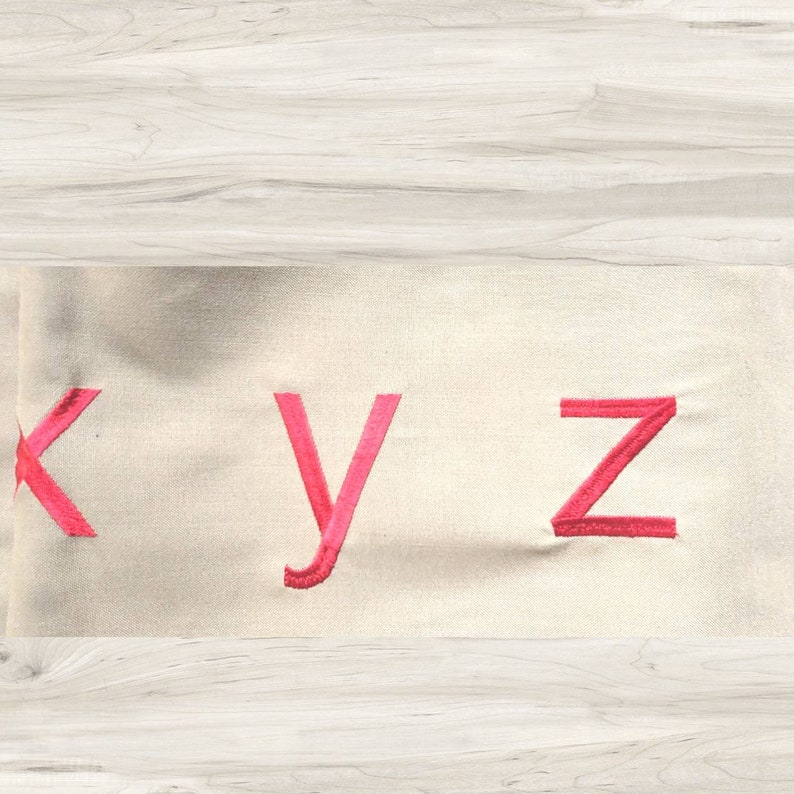 May include: A close-up of a white fabric with the letters "K", "Y", and "Z" embroidered in pink.