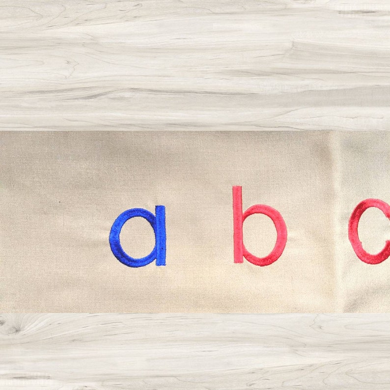May include: A close-up of a beige fabric with the letters "a", "b", and "c" embroidered in blue and red.